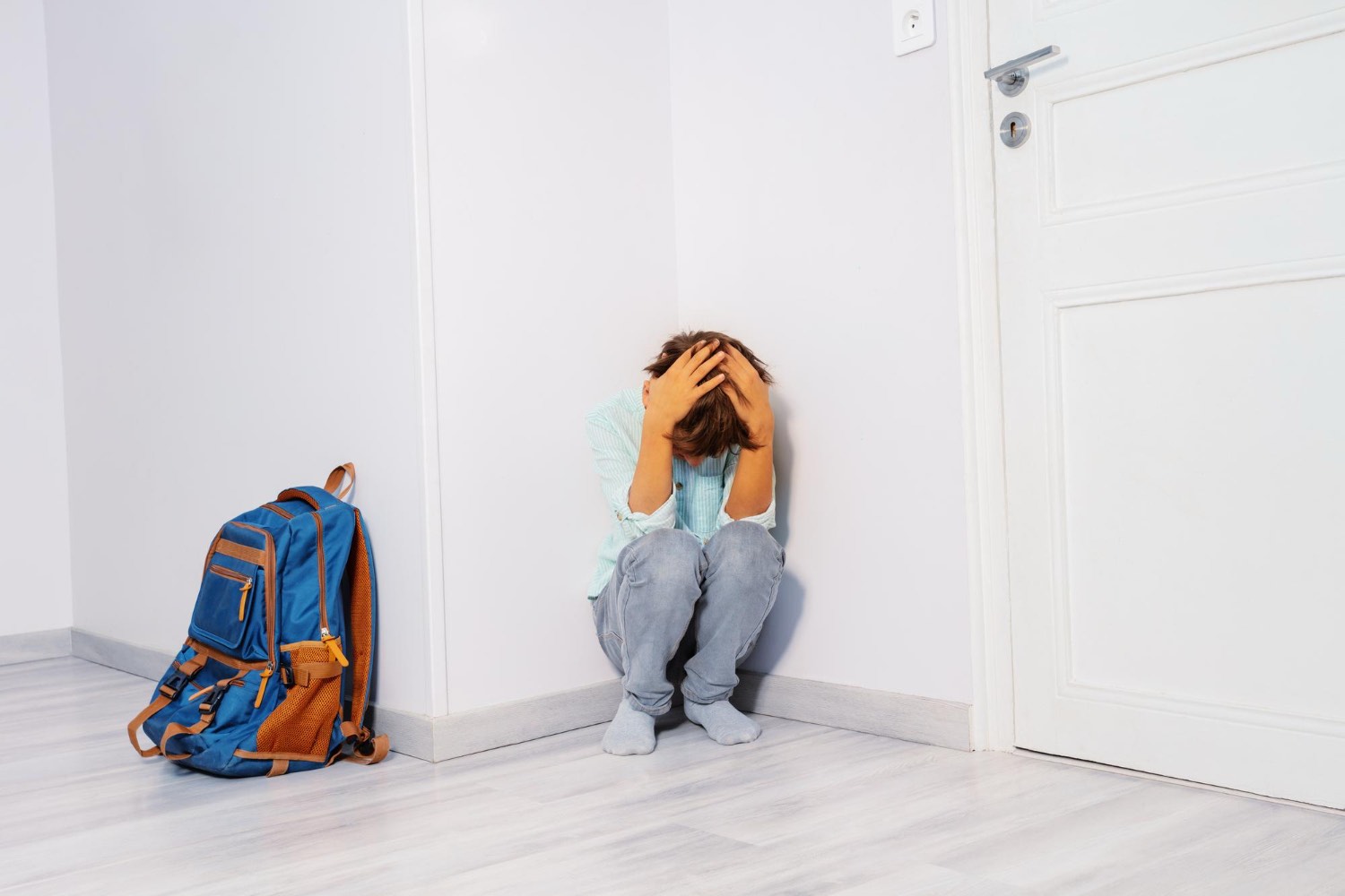 School anxiety Sunshine Coast, distressed child sitting in a corner with head in hands next to a school backpack