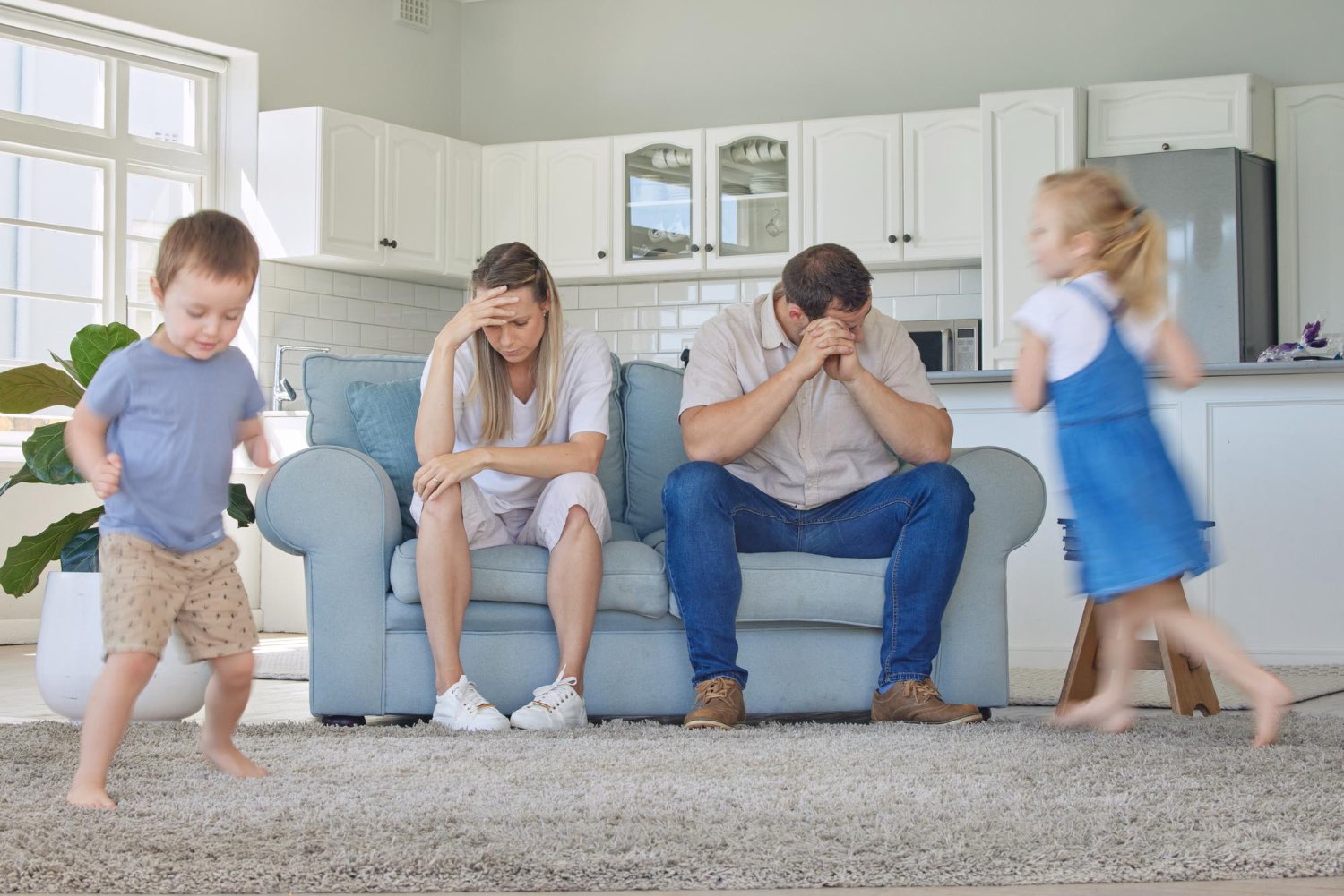 Parent burnout and anxiety depicted by exhausted parents sitting on a couch with children running about