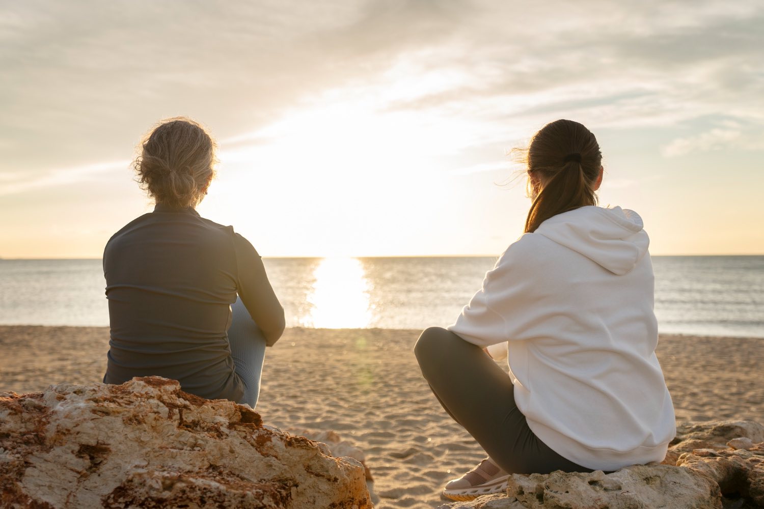 Two people sitting on a beach looking at the sunset illustrating how anxiety and mood can change in winter on the Sunshine Coast
